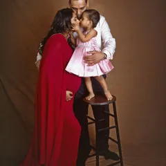 A moment of pure family love. The parents-to-be share a kiss with their daughter, who stands on a stool to reach them. It's a perfect capture of a family growing with love.