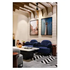 The waiting lounge features a mix of furniture styles and a bold color palette. The deep blue sofa contrasts with the patterned floor, while framed photos of Canadian cityscapes connect the space to the college's origins.