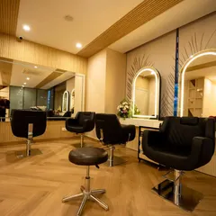 This view shows the arrangement of styling chairs and mirrors, designed for both client comfort and stylist efficiency. The herringbone-patterned flooring and subtle wall details contribute to the salon's modern yet timeless aesthetic.