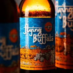 This shot of Flying Buffalo beer uses dramatic lighting to highlight the rich amber color of the lager and the fine condensation on the bottle, making it look incredibly refreshing.