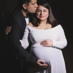 A tender moment captured in the studio with dramatic lighting. The partner kisses the mother-to-be's forehead in this gentle and loving portrait.