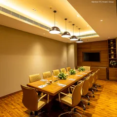A wider perspective of the boardroom highlights its spacious layout and professional ambiance. The warm wood tones and modern lighting are designed to create a comfortable yet formal setting for executive meetings and corporate presentations.