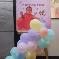 This custom welcome board was created for a butterfly and fairy-themed first birthday. It features a picture of the birthday girl and is surrounded by pastel balloons to match the party's color scheme.