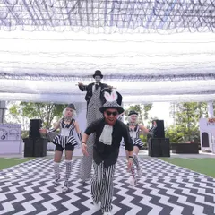 Performers on stilts and in whimsical black-and-white costumes entertain guests on a chevron-patterned runway, bringing the 'Line Art Carnival' to life.