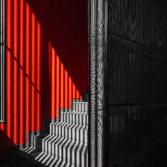 Light and shadow create a dynamic pattern on the staircase of Project 1374. The bold red wall contrasts with the dark, charred wood and the textured concrete, showcasing our approach to creating a rich, layered tapestry of materials.