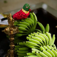 A detail from our styling workshop, showcasing a traditional brass lamp and a parrot crafted from cloth and beads, resting on a bunch of green bananas. It's all about finding beauty in unexpected combinations.