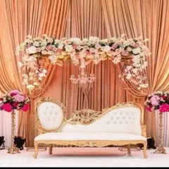 I design elegant reception stages perfect for classic weddings. This setup features a beautiful floral arch, a vintage-style diwan sofa, and soft golden lighting for a timeless and romantic feel.