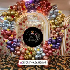 A beautiful circular ring backdrop for a 25th anniversary. The ring is covered in multi-colored chrome balloons, with a "Happy Anniversary" neon sign glowing in the center, creating an ideal photo point.