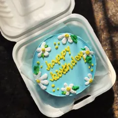 A bright and cheerful birthday bento cake. The sunny blue frosting is adorned with hand-piped daisies and a happy yellow "happy birthday" message.