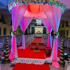 A breathtaking view down the aisle towards the wedding mandap. The entrance is framed by a canopy of pink and white drapes and flowers, creating a grand and romantic pathway for the ceremony.