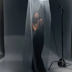 An experimental studio portrait using a sheer curtain and a single light source. The image plays with transparency and shadow to create a dramatic and ethereal effect.