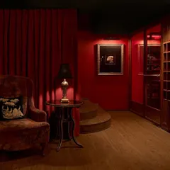The foyer of the ZLB23 speakeasy, where deep red walls and a plush velvet armchair create an atmosphere of vintage luxury. The design guides guests through a series of unfolding spaces, building anticipation.