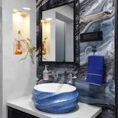 This wash area uses a vibrant blue patterned ceramic basin as its centerpiece. The wall behind features a swirling blue and black pattern, complemented by a decorative wrought-iron mirror frame.