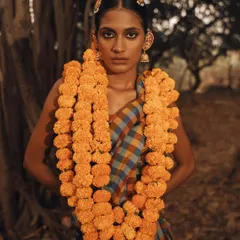 A powerful portrait from a conceptual outdoor shoot titled "Deivīgam" (Divinity). The model is adorned with marigolds, connecting her to themes of nature, tradition, and spirituality.
