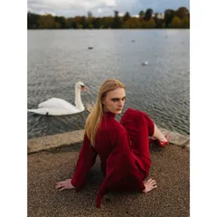 An on-location editorial shoot in London. The vibrant red of the dress contrasts with the natural, muted tones of the lakeside setting, creating a powerful and atmospheric fashion story.