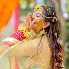 A candid moment of pure bliss during a Haldi ceremony. The bride, adorned with floral jewelry, laughs with joy as she is covered in turmeric and flower petals by her loved ones.