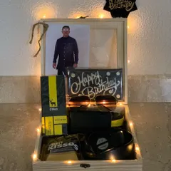 Celebrate him with a personalized wooden keepsake box. This birthday hamper includes a custom photo, a 'Happy Birthday' chocolate bar, stylish sunglasses, a wallet, and other treats, all beautifully arranged and lit with fairy lights.