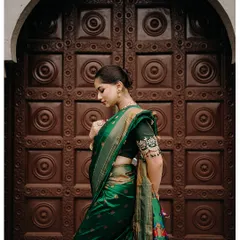 Elegance is timeless. A beautiful profile shot of the bride in her green silk saree, standing before a traditional carved wooden door.