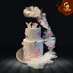 A magical two-tier butterfly cake perfect for a dreamer. This design features delicate edible butterflies fluttering up a cascade of white feathers, creating a light and ethereal look.