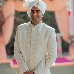 A simple, happy portrait of the groom in his elegant white sherwani, his smile full of warmth and anticipation for the ceremony.