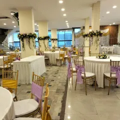 This image shows a large hall set for a 60th-anniversary celebration, featuring a cream and lavender color scheme. We manage everything from the chair sashes to the floral arrangements on the pillars to create a cohesive look.