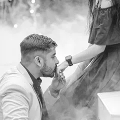 A chivalrous and tender moment captured in classic black and white. The groom kissing the bride's hand is a timeless gesture of love, made even more powerful by the dramatic, smoky background.