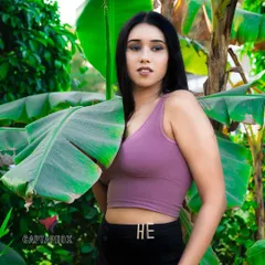 A medium close-up outdoor portrait set against vibrant green banana leaves. The natural lighting and background create a fresh, tropical feel that complements the model's casual top and simple styling.
