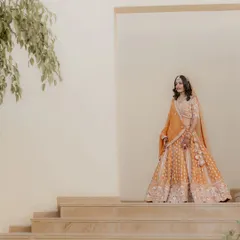 A full-length bridal portrait showcasing the magnificent orange lehenga against a minimalist architectural backdrop. This shot is all about grace and style.