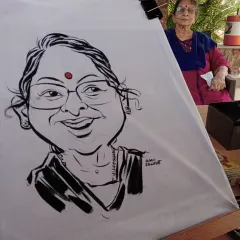 A freshly painted caricature on a t-shirt, with the smiling subject sitting right behind it. I paint these live for guests to watch.