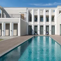 The clean geometry of this modern-classical facade is softened by the tranquil blue of the swimming pool. We design homes as complete experiences, where every exterior view is composed with artistic intent.