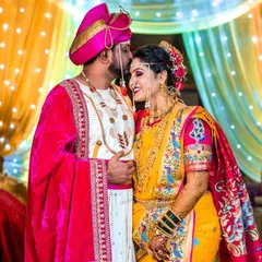 A tender moment between the bride and groom in their full Maharashtrian wedding attire. The groom's traditional velvet robe and the bride's embroidered yellow saree create a rich, colorful palette.