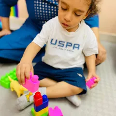 A toddler concentrates on stacking colorful blocks, an essential play activity for developing spatial awareness, fine motor skills, and an early understanding of physics.