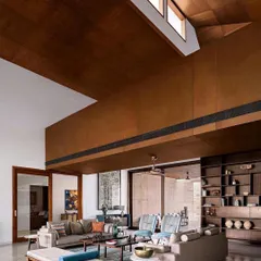 The double-height living room in this Ahmedabad home features a dramatic wooden-clad ceiling and clerestory windows that fill the space with soft, indirect sunlight.