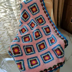 The Lydia blanket draped over a chair, showing how the soft pink fabric and colorful squares can brighten up a room.