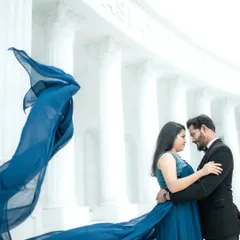 A dramatic, cinematic shot featuring a flowing blue gown against the grand, all-white architecture of a studio set. This style is perfect for couples who dream of a filmi, larger-than-life pre-wedding album.