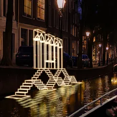 A closer view reveals how the installation's layered arches and steps descend towards the water, mirroring the form of a traditional Indian step-well. The reflection in the canal completes the illusion, creating a full, immersive form from light alone.