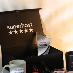 An angled view of the Airbnb "Superhost" gift box, showing the personalized trophy, branded mug, and other curated items nestled inside. The presentation is designed to feel exclusive and celebratory.