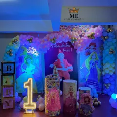 A grand Disney Princess theme for a first birthday party. The stage is decorated with character backdrops of Cinderella and Rapunzel, a balloon arch, 'BABY' blocks, and a light-up number '1'.