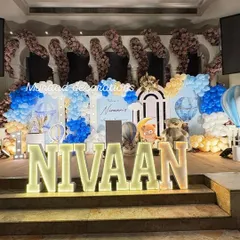A wider view of the stage for Nivaan's Mundan ceremony. This shot captures the full scale of the decoration, including the floral arrangements at the top and the detailed hot air balloon themed backdrop.