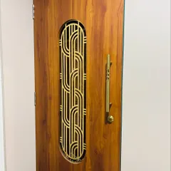 A close-up of a wooden safety door with an elegant, interwoven brass grill design. The long brass handle complements the grill and adds a touch of luxury.