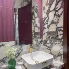 Color can completely transform a small space. Here, I paired bold magenta wall tiles with heavily veined black and white marble. The arched mirror softens the look, while the gold faucet adds a touch of warmth and luxury to this vibrant powder room design.