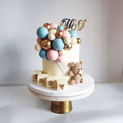 A classic and beautiful baby shower cake for a lovely couple. This design features a teddy bear holding a cascade of pink, blue, and gold chocolate balloons, with edible 'BABY' blocks.