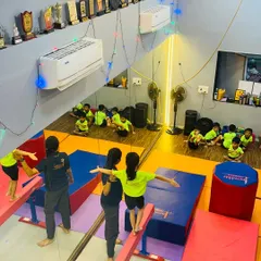A bird's eye view of a typical gymnastics class at our Gorai studio. You can see children practicing on low balance beams with instructor assistance, while others wait their turn, showcasing our structured and supervised class environment.
