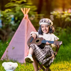 A sweet and candid moment during an outdoor shoot. This little girl is enjoying a song on her ukulele, sitting in front of a teepee with her teddy bear by her side.