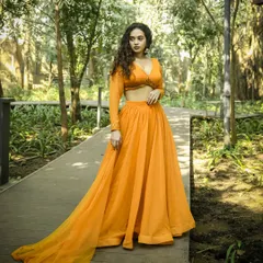 A full-length shot that establishes the scene. The long train of the skirt is elegantly displayed along the wooden pathway, giving a sense of grandeur to this modern ethnic outfit. This type of image is perfect for a campaign's opening shot.
