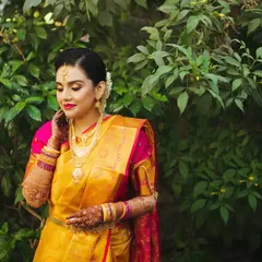 A radiant South Indian bride in her traditional yellow and pink silk saree. This outdoor portrait against a lush green background highlights the vibrant colors and her natural elegance.