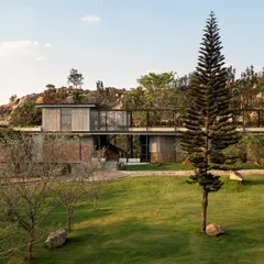 'The Earth' project, viewed from a distance, appears to emerge from the green landscape, with its clean lines and material choices complementing the rocky hills behind it.