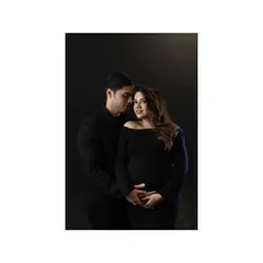 An intimate and classic couple portrait. The dark outfits and background create a moody, dramatic feel, while the close embrace and her gentle look towards the camera make it a powerful and connecting image.