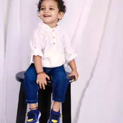 A simple and classic portrait of a toddler with a bright smile, sitting on a stool against a clean white backdrop. Sometimes the simplest setups are the most beautiful.