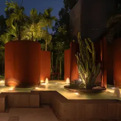 The KEUS commercial landscape at night, where strategic lighting transforms the space. The illuminated Corten steel walls, cacti, and water fountains create a dramatic and inviting atmosphere for evening events and showcases.